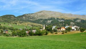 A picturesque alpine village nestled in green fields and hills under a clear blue sky.